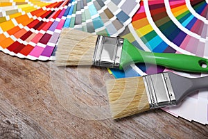 Paint brushes and color palette samples on wooden background