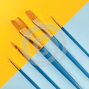 Paint brushes on diagonally yellow and blue background. Square.