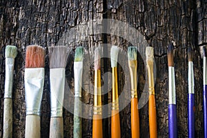 Paint brushes of different sizes have different colors in a row horizontally on an old wooden