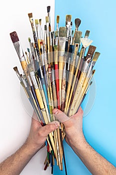 Paint brushes in male hands on a colored background, top view.