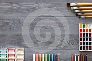 Paint brushes, paintbox with watercolors, crayons, pencils on grey wooden background, art table. Top view with copy space photo