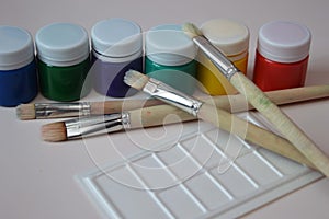 Paint brushes and a row of closed jars of colored gouache paints. Set for creativity and hobby