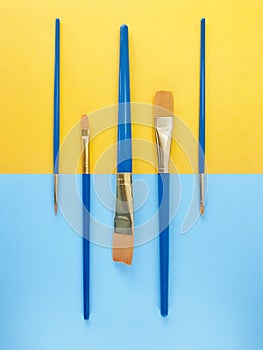 Paint brushes towards opposite on yellow and light blue background. vertical.