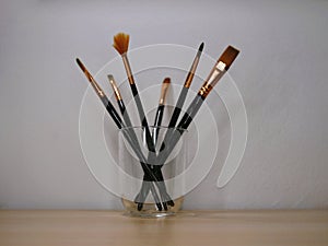 Paint brushes in a transparent glass at the background of a white wall