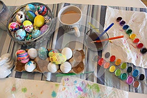 Paint and brushes with water and paper towels on a table with a bowl of easter eggs