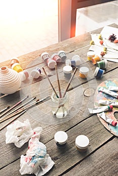 Paint brushes in a water and scattered containers with poster paints