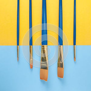 Paint brushes on yellow and light blue background. Square.