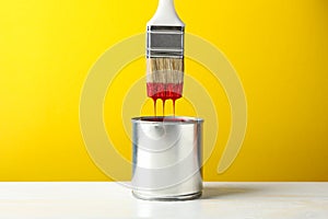 Paint can and brush against yellow background