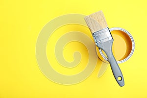 Paint can and brush on yellow background, top view.