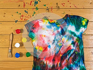 Paint cans with a brush and a tie dye t-shirt on a wooden table. Flat lay.