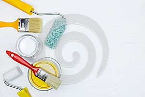 Paint cans, brushes, paint rollers on white wooden desk surface