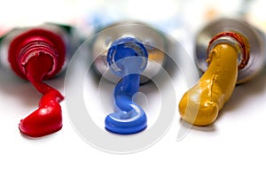 paint colors in yellow, blue and red flowing from the tubes, closeup on white with copy space