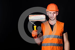 Paint and renovate concept. Decorator painting wall, copy space. Man in helmet, hard hat holds paint roller, black