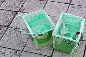 Paint roller and brush in a bucket with an emulsion on concrete paving, front and background blurred with bokeh effect