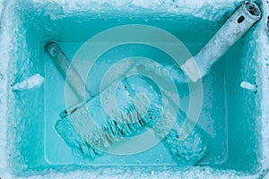 Paint roller and brush in a bucket with an emulsion on concrete paving, front and background blurred with bokeh effect