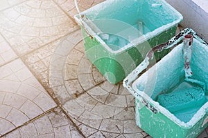 Paint roller and brush in a bucket with an emulsion on concrete paving, front and background blurred with bokeh effect