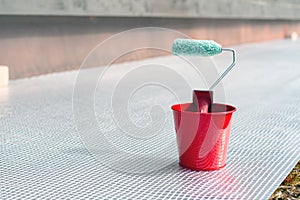 Paint roller and a bucket with paint next to a building exterior wall. Painting house plinth outside. Home renovation. Nobody