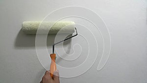 Paint roller with orange handle on white wall