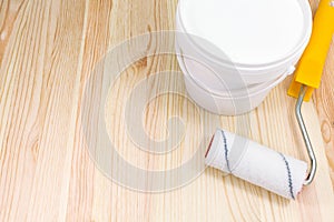Paint roller with paint can on wooden background