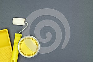 Paint roller with paint tray and can of yellow paint on ultimate gray background. flat lay