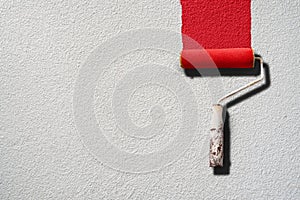 Paint roller painting with red paint on white wall photo