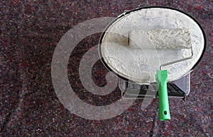 A paint roller soaked with white color and put on the lid of a paint container with lot of copy space. The equipment is placed on