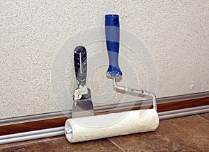 Paint roller and trowel stands in a room at baseboard near wall