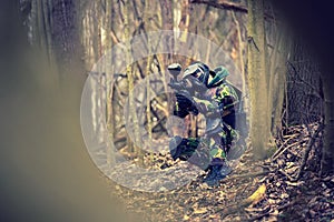 Paintball player in protective uniform and mask aiming gun in th