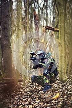 Paintball player in protective uniform and mask aiming gun in th