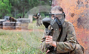 Paintball players of one team in camouflages and masks aiming with gun in shootout playing