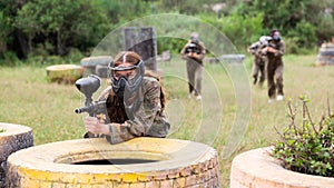 Paintball players of one team in camouflages and masks aiming with gun in shootout playing