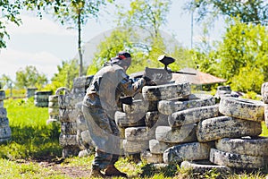 Paintball sport player in protective uniform and mask playing with gun outdoors.