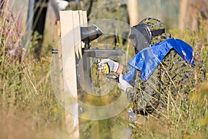 Paintball sport player in protective uniform and mask playing and shooting with gun outdoors.