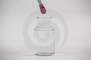 Paintbrush with pink paint dipped into a jar filled with water
