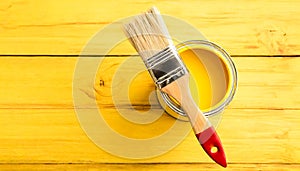 A paintbrush is sitting in a can of yellow paint. The brush is red and white. Concept of creativity and the idea of painting