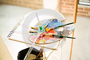 Paintbrushes on artist canvas covered with oil paint with palette closeup