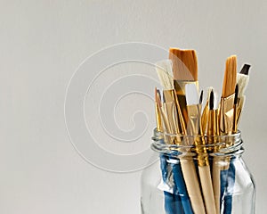 Paintbrushes in a glass jar isolated on grey background.