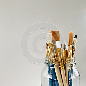 Paintbrushes in a glass jar isolated on grey background. Square.