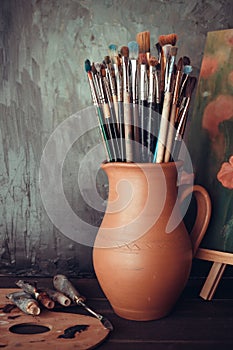 Paintbrushes in jug, palette, paint tubes and painting