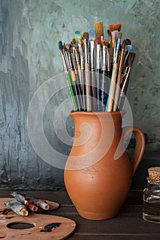 Paintbrushes in a jug from potters clay, palette and paint tubes photo