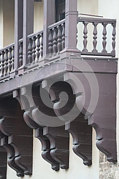 Painted brown scalloped wood brackets, shaped pickets, railing, and columns on veranda