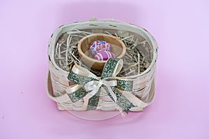 THe painted colorful Easter egg in the basket on the pink background copyspace