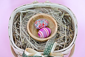 THe painted colorful Easter egg in the basket on the pink background copyspace