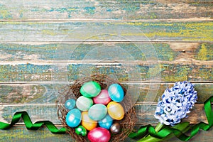 Painted colorful Easter eggs in nest with hyacinth flowers and ribbon top view. Festive background for spring holiday.