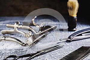 On a painted concrete surface are old hairdresser tools. two vintage hand-held hair clipper, hairdressing scissors