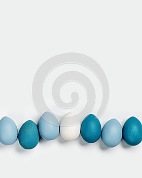 Painted Easter eggs blue, gray colored in row on white background with copy space. Chicken egg natural pastel shades