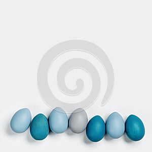 Painted Easter eggs blue, gray colored in row on white background with copy space. Chicken egg natural pastel shades