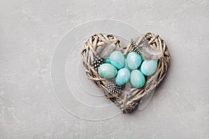 Painted Easter eggs in heart nest on vintage background top view in flat lay style.