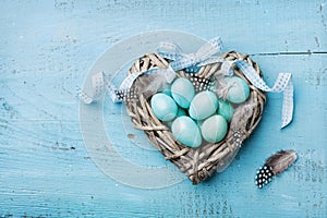 Painted Easter eggs in heart nest on vintage turquoise background top view in flat lay style.