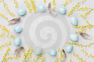 Painted Easter eggs, mimosa flower and feather on vintage stone background top view in flat lay style. Clean space for text.